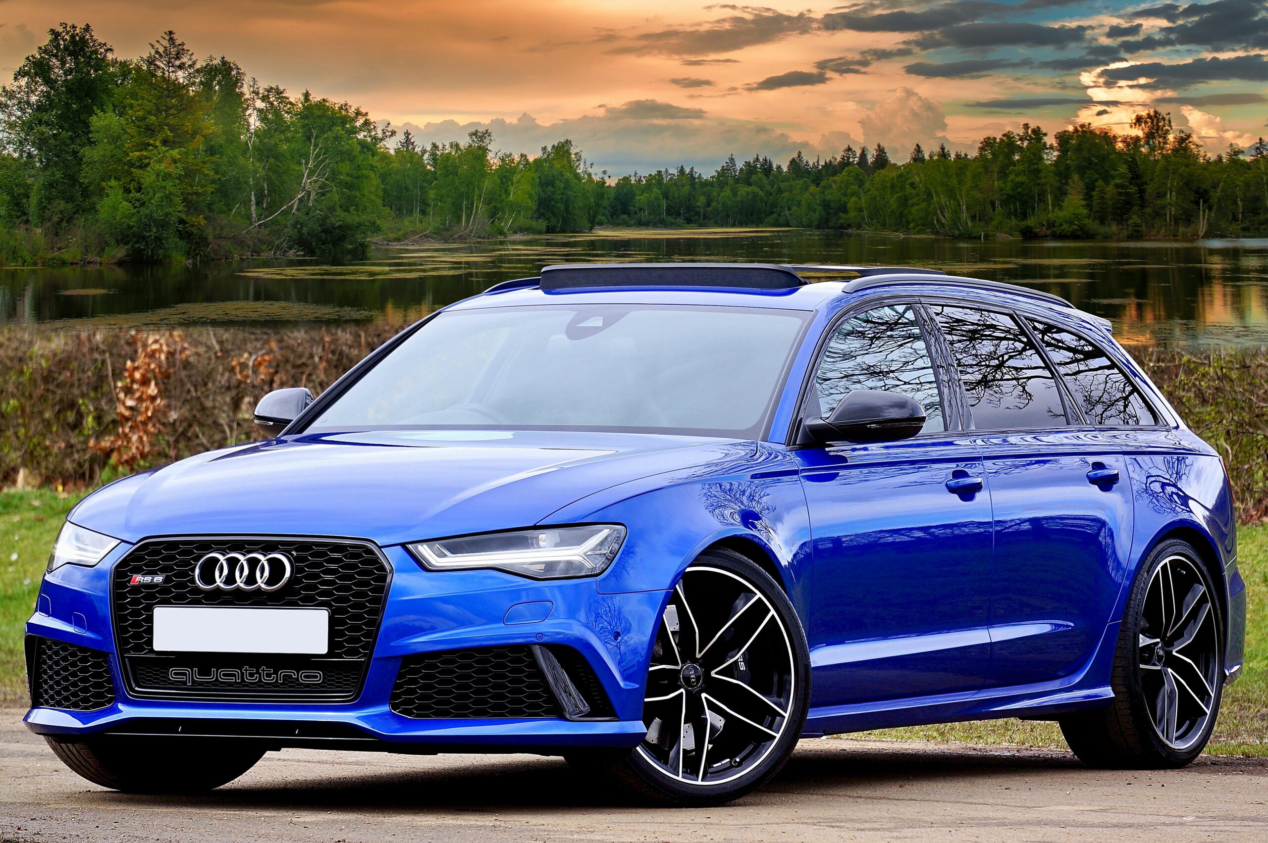 Offerings A modern blue Audi RS6 parked by a lake with scenic forest and sky backdrop.